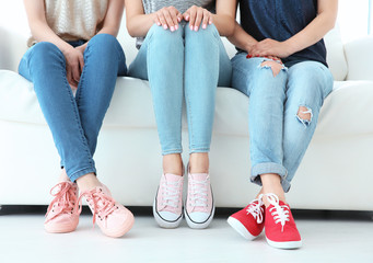Young women with beautiful legs in jeans and sneakers sitting on sofa