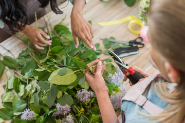 Fototapeta premium cropped shot of young florists arranging beautiful flowers and green leaves in flower shop