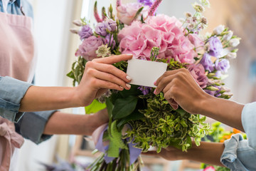 close-up partial view of female hands holding blank business card and bouquet of beautiful flowers