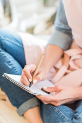 close-up partial view of young woman in apron writing in blank notebook with pen