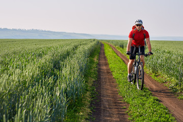 Young cyclist riding bicycle on the road on green field.