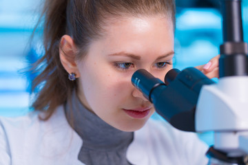 Young woman scientist looking a microscope in a laboratory. Girl scientist doing microbiological research