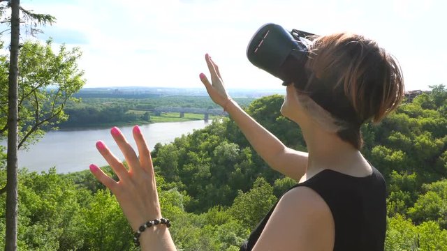 Young woman uses head-mounted display in the park. Playing game using VR-helmet for smart phones