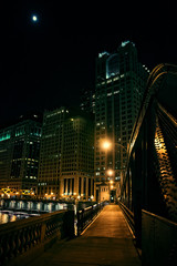 Fototapeta na wymiar Dark city steel bridge and river promenade at night in Chicago. Surreal urban scene with the moon over skyscrapers.