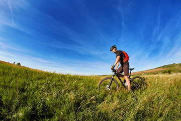 Fototapeta premium Young cyclist riding mountain bicyclist against beautiful sunset in the countryside.