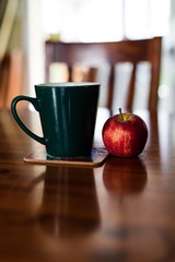 Green coffee cup and an apple on a reflective wooden table