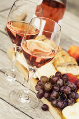 Two glasses of rose wine and board with fruits, bread and cheese on wooden table
