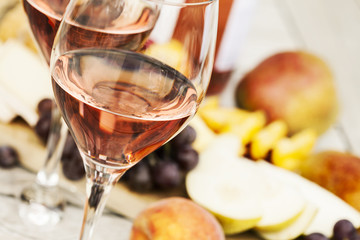 Two glasses of rose wine and board with fruits, bread and cheese on wooden table