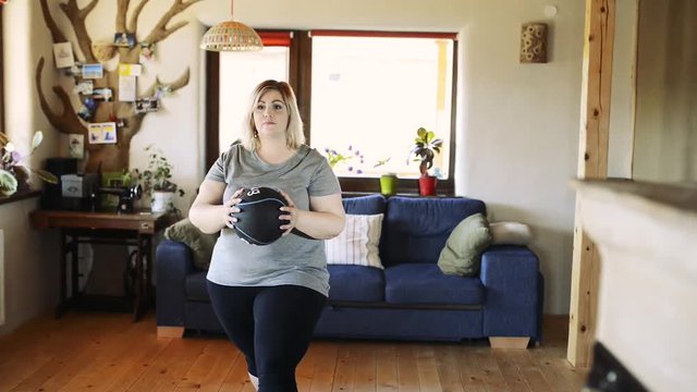 Attractive overweight woman at home working out with medicine ball.