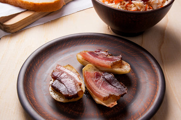 Close up view of baked potatoes with slices of bacon on wooden background. Sauerkraut in clay bowl and slices of white bread on cutting board.