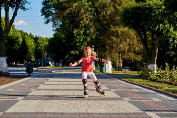 Pretty little girl in red cloth learning to roller skate outdoors on beautiful summer day in city park.