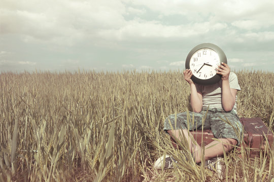 Boy on a trip hides his face with a clock in a desert landscape