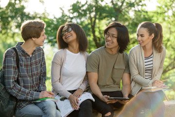 Happy young students sitting studying outdoors