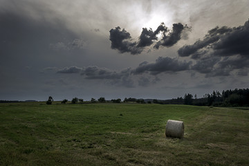 bale of hay in a meadow under storm clouds with forest in the background at sunset
