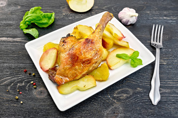 Duck leg with apple and potatoes in plate on black board