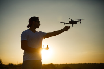 Silhouette of a man catching drone with one hand and remote controller in another hand on sunset....