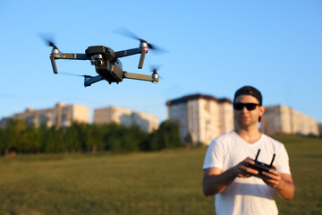 Compact drone hovers in front of man with remote controller in his hands. Quadcopter flies near pilot. Guy taking aerial photos and videos from above