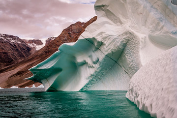 Iceberg reflecting the green sea with glacier, snow and a pink sky behind. © Di