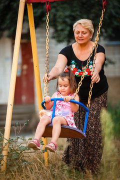 Grandmother Pushing Granddaughter On Swing In Park