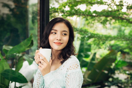 Pretty vietnamese woman enjoying her morning coffee on a veranda