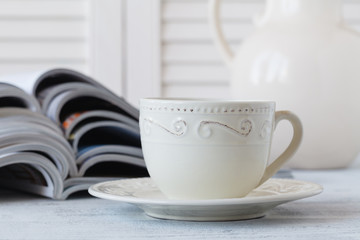 Stack of magazines and white cup of coffee on white background.