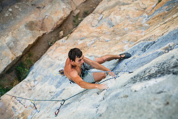 sports man climbs an overhang rock near forest and grip the hold