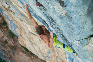 sportsman Dmitrii Fakirianov climbs an overhang rock and makes a long move
