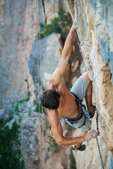 sports man climbs an overhang rock near forest and put the rope into sling