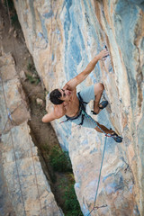 sports man climbs an overhang rock near forest and put his hand into magnesia bag