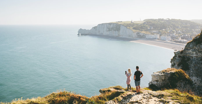 Love couple hiking and taking picture of Etretat cliffs and Atlantic ocean in Etretat, France
