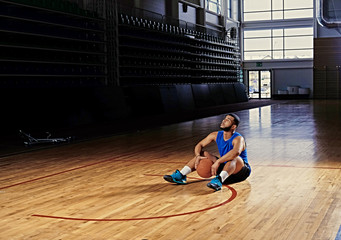 Black professional basketball player sits on a floor in a game hall.