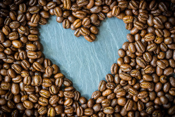 Pea berry coffee beans with heart shape on nature stone plate , top view and copy space