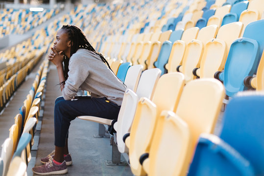 The horizontal side view of the nervious afro-american girl observing the match while leaning on the knees. The stadium location.