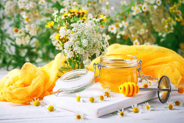 Tasty and healthy honey on white wooden table with flowers of chamomile.