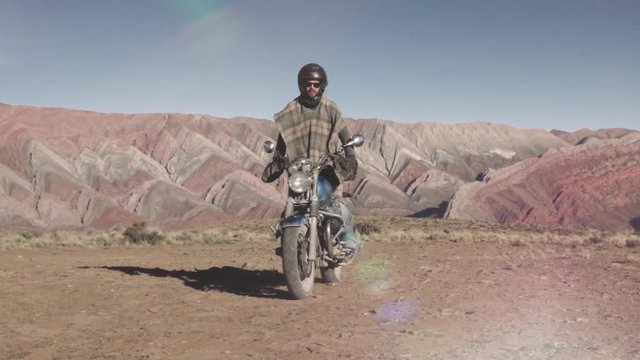 Man riding custom motorcycle on a dirt road, on the background the rainbow mountain.Slow motion	