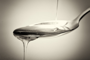 Honey pouring from spoon against a light background