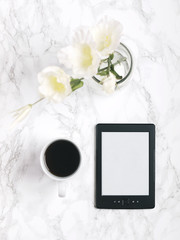 Tablet or e-reader with white flowers and black coffee on white marble background. Flat lay. Top view. Copy space.