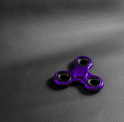 Purple fidget spinner toy. backdrop is Genuine black leather ,focus on device. Close up , photo...