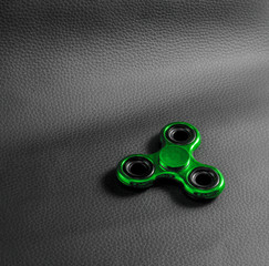 Green fidget spinner toy. backdrop is Genuine black leather ,focus on device. Close up , photo from...