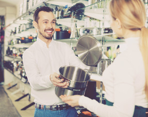 Male shop assistant helping customer to choose saucepan