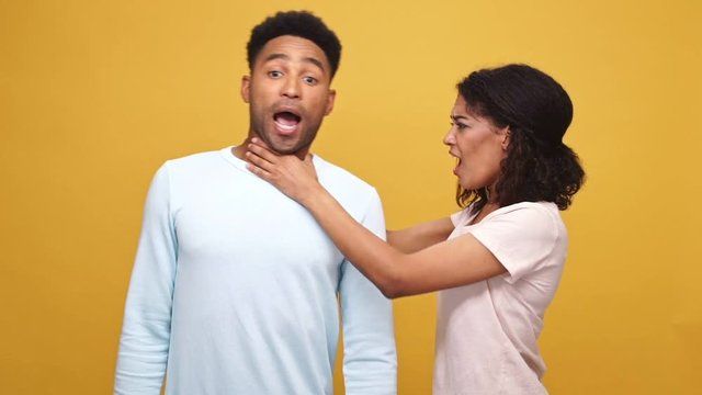 Angry young african woman strangling her boyfriend isolated over yellow background