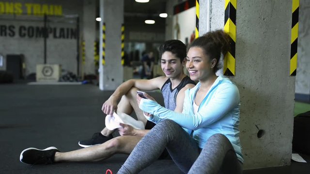 Young fit couple in gym resting, watching pictures in smartphone.