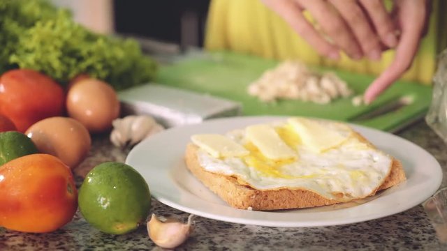 Bread with fried egg, plate on kitchen table. Putting cheese slices on top for sandwich. Other ingredients around (eggs, lettuce, tomatoes, lime, garlic, pack of cheese) Shot with Sony a7s on tripod