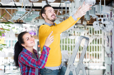 man and girl in lighter shop choosing modern round glass ceiling lamp for house