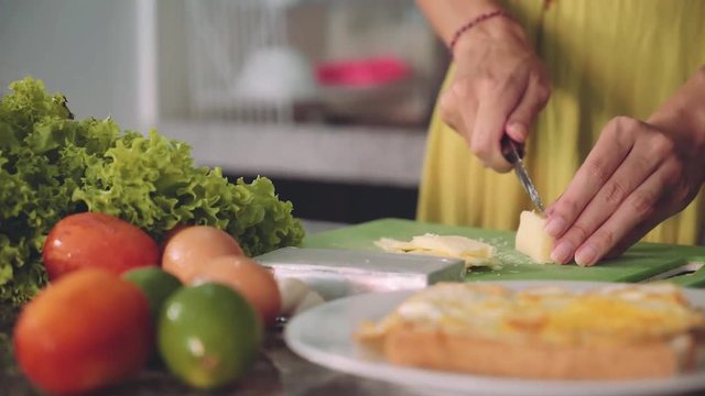 Cutting soft cheese for sandwich on a kitchen table. Tomatoes, eggs, lime, lettuce and plate with bread and fried egg in the foreground, Shot with Sony a7s on a slider