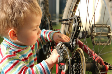 Boy repairing a bicycle chain near the inverted bicycle wheel - obrazy, fototapety, plakaty