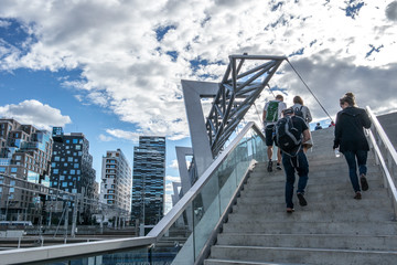 People walking over bridge to the business area at Bjørvika in Oslo, Norway with a modern Scandinavian architecture with glass windows