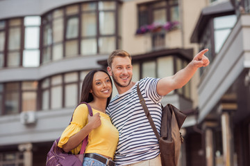 young happy multiethnic couple of tourists walking in city, man pointing somewhere