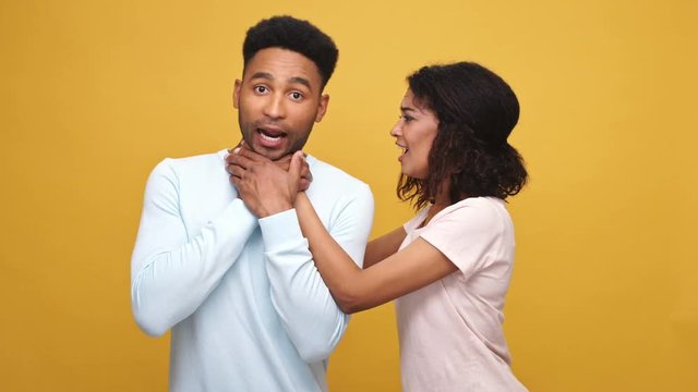 Violent young african woman strangling her boyfriend isolated over yellow background