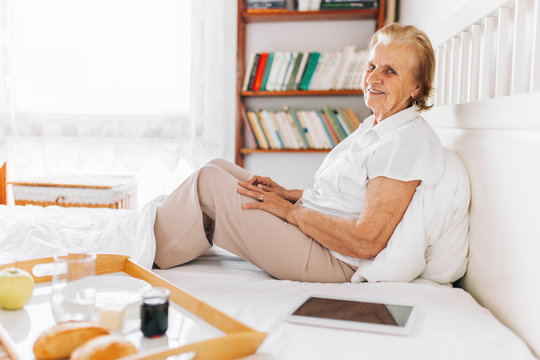 Elderly woman having breakfast in bed whilst using her tablet